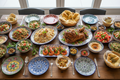 Wooden table covered in Middle eastern dishes on colourful ceramics including rice dishes, lamb, prawns, flatbreads and summertime salads